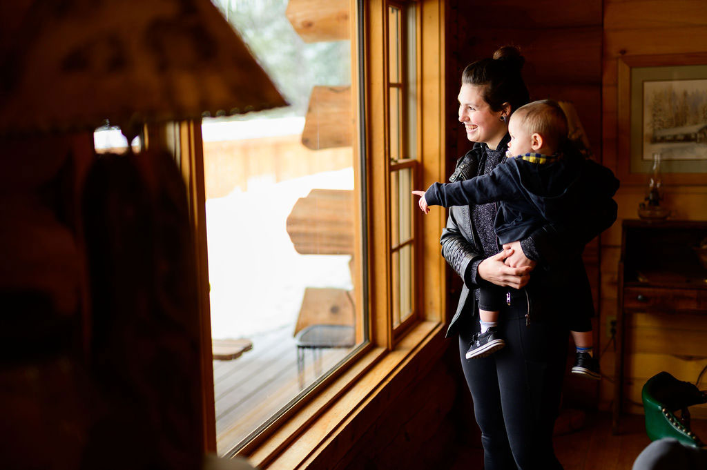 A mom and her baby looking out the larger lodge window at the snow